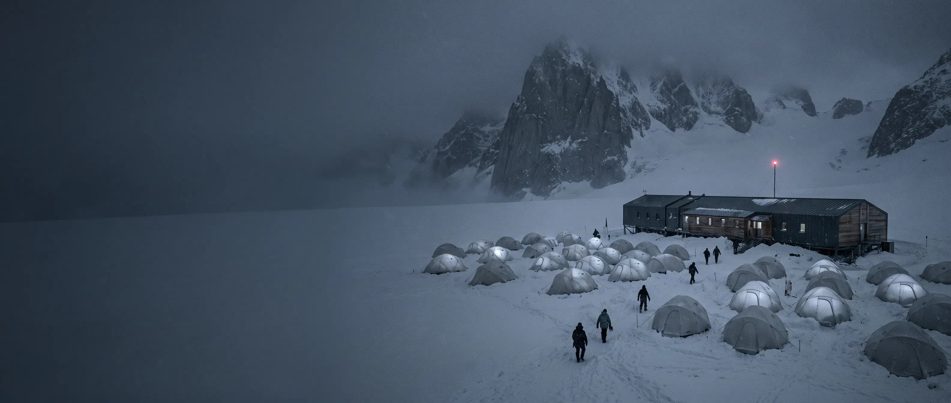 A base camp of lit tents on a snowfield below a mountain range, its paths leading to one hall with a red beacon